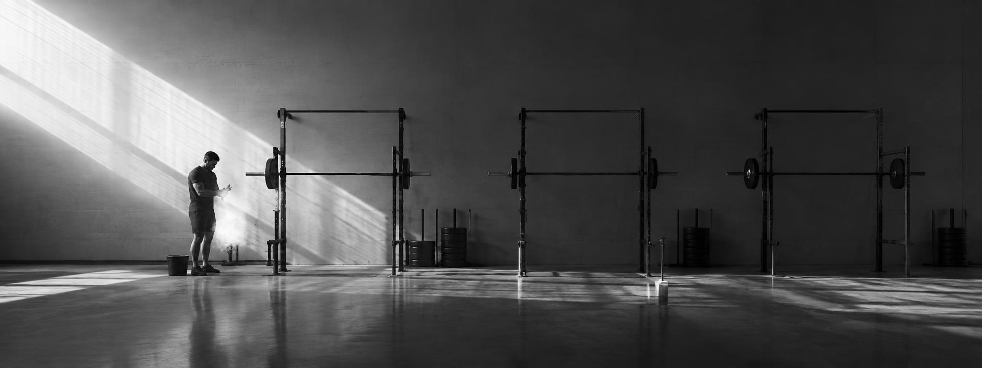 Wide view of a concrete strength gym with squat racks and an athlete chalking up