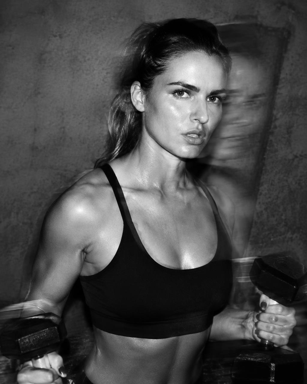 Athlete holding dumbbells under hard flash against concrete